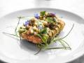 Closeup shot of a fried biscuit with caviar, corn and vegetable leaf on top in a white round plate